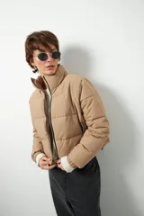 Campera puffer corta color beige de nylon, con cuello alto, cierre frontal y bolsillos laterales con cierre.