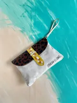 Sobre de mano Carolina de Cunto modelo Saria, confeccionado en cuero blanco con solapa de cuero animal print y detalle de tira amarilla. Cuenta con correa de muñeca, cierre con broche imán y arte pintado a mano en el frente.