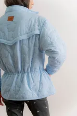 Campera reversible de estilo parka, color celeste, con diseño capitoneado con patrón de flores. Presenta ajuste elástico en la cintura, cuello alto y mangas largas. Incluye parche de marca en la parte superior de la espalda.