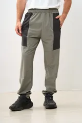 Pantalón deportivo gris con paneles laterales negros, cintura elástica y puños ajustados.