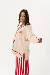 Saco oversize tejido con ilustraciones inspiradas en corales, peces, estrellas de mar y tortugas. Presenta galón picot en rojo en cartera y puños, y botones a tono.