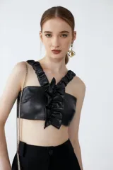 Top corto de cuero sintético negro con breteles fruncidos con elástico y volado central. Espalda unida por tiras elastizadas y fruncidas.