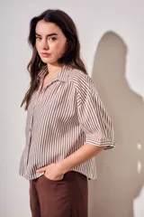 Camisa de corte oversize con estampado de rayas verticales en tonos marrón y beige. Presenta cuello camisero, cierre frontal con botones y mangas cortas con caída relajada.