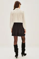 Falda corta de color negro con diseño plisado y detalle de volado en el ruedo. Presenta una cintura ancha con apliques de tachas metálicas decorativas.