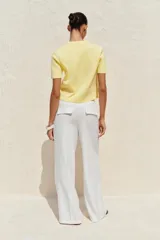 Chaqueta de punto color amarillo pálido, con cuello redondo, manga corta, cierre frontal con botones dorados y bolsillos de parche en el pecho.