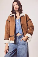 Campera marrón de gamuza sintética con cuello, puños y ruedo de piel sintética blanca. Presenta cierre frontal con cremallera, bolsillos laterales y detalles en cuero sintético negro.