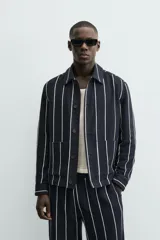 Sobrecamisa de hombre, corte relajado, color azul marino con rayas verticales blancas. Presenta cuello solapa, manga larga con puños abotonados, bolsillos de parche delanteros y cierre frontal de botones.