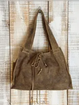 Bolso tipo tote de cuero con acabado craquelado en tonos blanco y beige. Presenta un diseño estructurado con doble asa superior y un cierre frontal mediante cordones de cuero con detalle de borlas.