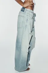 Jeans de tiro medio y corte baggy con cinco bolsillos, trabillas y rotos decorativos. Cuenta con detalle de cinturón confeccionado en el mismo tejido y cierre frontal con cremallera y botón metálico.