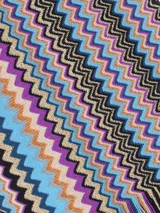 Chal o bufanda de punto con el icónico patrón de zigzag (chevron) de Missoni, en tonos tierra, negro, amarillo mostaza y azul claro. Presenta flecos en los extremos.