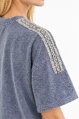 Remera oversize de algodón con acabado stonewash, color gris azulado, manga corta y cuello redondo. Cuenta con apliques bordados a mano en forma de hojas con canutillos plateados sobre los hombros.