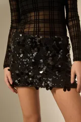 Falda mini de corte ajustado, completamente cubierta de lentejuelas negras circulares sobre una base de poliéster.