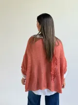 Sweater de punto color naranja con diseño holgado, que incorpora franjas horizontales de encaje con motivos florales. Presenta mangas tres cuartos con puños abotonados y se complementa con una bufanda del mismo tejido y color.