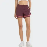 Short deportivo New Balance 2 en 1 para mujer, color bordó con ribetes en color coral. Confeccionado con tecnología NB DRY de secado rápido, incluye una calza interna para mayor soporte, bolsillos laterales y cintura elástica.