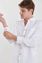 Camisa de vestir blanca de manga larga, con cuello abotonado, bolsillo frontal y botones en tono madera.