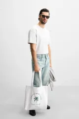 Bolso tipo shopper blanco de tela con asas de hombro. Estampado frontal con texto "Athletic Sports Club", una palmera y la frase "Embrace the lifestyle" con el año "Est. 1975".