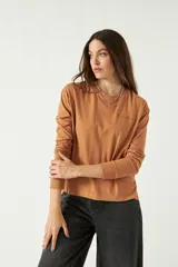 Remera de manga larga color marrón, con cuello redondo y bordado sutil en el pecho izquierdo. Presenta un corte recto con aberturas laterales en el ruedo.