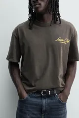 Camiseta de corte relajado con cuello redondo y manga corta. Presenta un efecto lavado y estampados a contraste en el frente y la espalda.