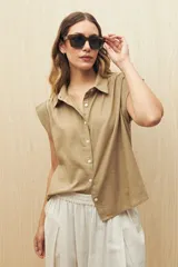 Camisa color beige, de corte recto, con cuello clásico, mangas cortas con volados en los hombros y cierre frontal con botones.