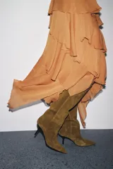 Bota de caña alta color verde oliva, confeccionada en serraje, con pespuntes decorativos y tacón tipo kitten. Acabado en punta.