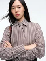 Camisa de manga larga con estampado de rayas verticales en tonos marrones y blancos. Presenta cuello clásico y cierre frontal con botones, acompañada por una corbata del mismo tejido y estampado.