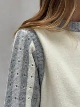 Sweater de lana color crudo con mangas largas abullonadas en gris y blanco, con diseño de rayas y perforaciones. Cuello redondo y puños acanalados.