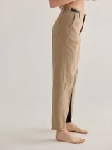 Pantalón de corte cigarette, tiro alto, color beige claro, con costuras visibles en contraste y detalle de panel interior negro visible en la abertura del tobillo. Presenta bolsillos delanteros y traseros, y elástico en la pretina trasera.