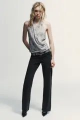 Top halter de tul color gris claro, con escote fluido drapeado y espalda descubierta. Presenta bordados con aplicación de abalorios en tonos oscuros y dorados.