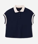 Chomba azul marino de corte boxy y manga corta, confeccionada en tejido piquet de algodón. Cuenta con cuello polo y ribetes en las mangas de color beige contrastante, además de una botonera frontal corta.