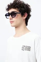 Remera blanca de corte amplio con mangas cortas y estampado con la frase "Unlearn" en el frente y gráfico en la espalda.