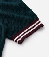 Polo de manga corta confeccionado en tejido de punto texturizado con trama vertical. Presenta cuello, puños y ruedo en color bordó con detalles de rayas blancas en contraste. Cuenta con una abertura frontal con tres botones.