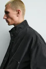 Cazadora relaxed fit confeccionada en tejido de algodón de color beige, con cuello subido y manga larga. Cuenta con bolsillos de plastrón en la cadera, bajo elástico y cierre frontal con cremallera oculta y alamares metálicos.