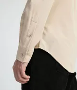 Camisa de manga larga color beige, con cuello camisero y dos bolsillos frontales con cierre en solapa.