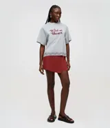 Short pollera corto color marrón rojizo, confeccionado en viscosa y poliamida, con diseño estructurado, canesú asimétrico en la cintura y efecto traspasado en la parte delantera.