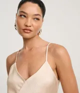 Vestido largo (midi) color beige claro, estilo slip dress, con escote en V y breteles finos ajustables. Presenta un recorte sutil en el área del busto.