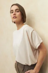 Remera color crema de manga corta y cuello redondo, con pliegues en los hombros y dobladillo en las mangas.