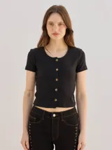 Remera negra de canalé ajustada al cuerpo, de manga corta y cuello redondo, con cierre frontal de botones metálicos.
