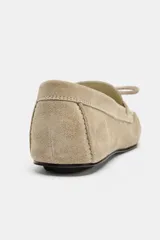 Mocasín plano de serraje color beige, con detalle de fruncido y lazo en la parte delantera y punta redonda.