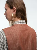 Chaleco estructurado de denim color terracota, con escote en V, cierre frontal con botones y bolsillos laterales tipo ojal.