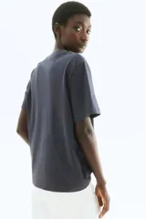 Remera de manga corta, cuello redondo y corte holgado, color gris oscuro o negro lavado, con estampado frontal en blanco que dice "CANNES 1980" y debajo "La Côte D'azur".