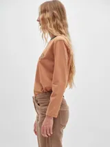 Remera de manga larga con cuello redondo y estampado a rayas horizontales en tonos marrón y negro. Tiene un logo bordado en el pecho de color rojo.