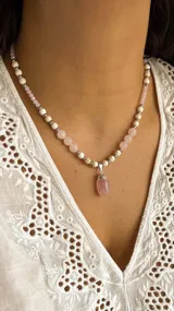 Collar de cuentas con dije colgante de cuarzo rosa pulido en forma de lágrima. El collar está compuesto por cuentas de cuarzo rosa de 8 mm, cuentas de piedra reconstituida de 6 mm y pequeñas cuentas metálicas plateadas.