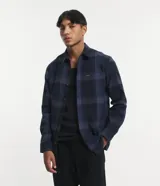 Camisa de manga larga con diseño de cuadros en tonos marrones, confeccionada en algodón. Presenta cuello camisero, cierre frontal con botones y un bolsillo en el pecho con botón.