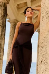 Vestido largo color chocolate con tirantes finos, escote recto y detalle de nudo en la cintura que crea una abertura en la falda.