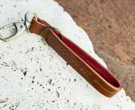Llavero de cuero en formato de tira con diseño minimalista, confeccionado en cuero genuino marrón con interior en contraste color fucsia, pespuntes rosados y herrajes metálicos envejecidos con gancho tipo mosquetón.