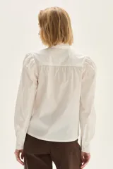 Camisa blanca de popelina elastizada con cuello alto con volados y mangas voluminosas.
