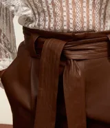 Short de cuero sintético color marrón, de tiro alto, con trabillas en la cintura, pliegues delanteros, bolsillos tipo cuchillo y cinturón para lazo.