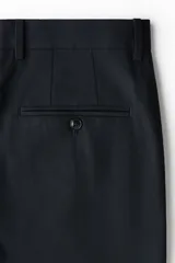 Pantalón sastrero de corte slim fit y diseño liso, color negro, con pliegues frontales, bolsillos laterales y cierre con botón.