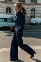 Jeans de denim azul oscuro, tiro alto, corte recto y pernera ancha, con raya planchada marcada en el frente y la espalda. Presenta cinco bolsillos y cierre frontal con botón dorado.