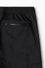 Pantalón cargo negro de nylon, corte recto y holgado, con cintura elástica y cordón ajustable. Presenta bolsillos cargo grandes en las piernas, bolsillos laterales y traseros con cierre, y cordón ajustable en los bajos.